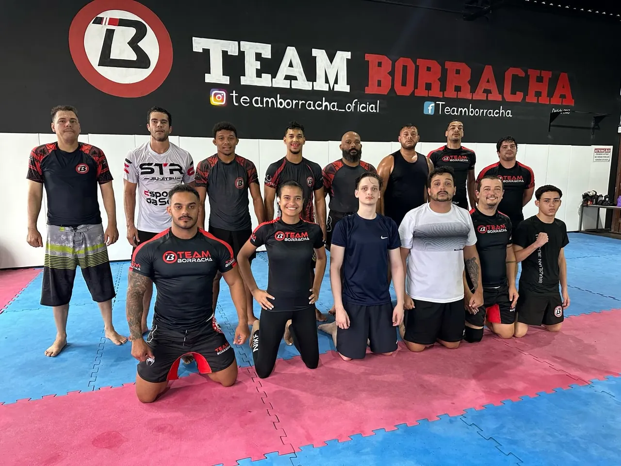 Equipe da Team Borracha reunida no tatame com o logo ao fundo